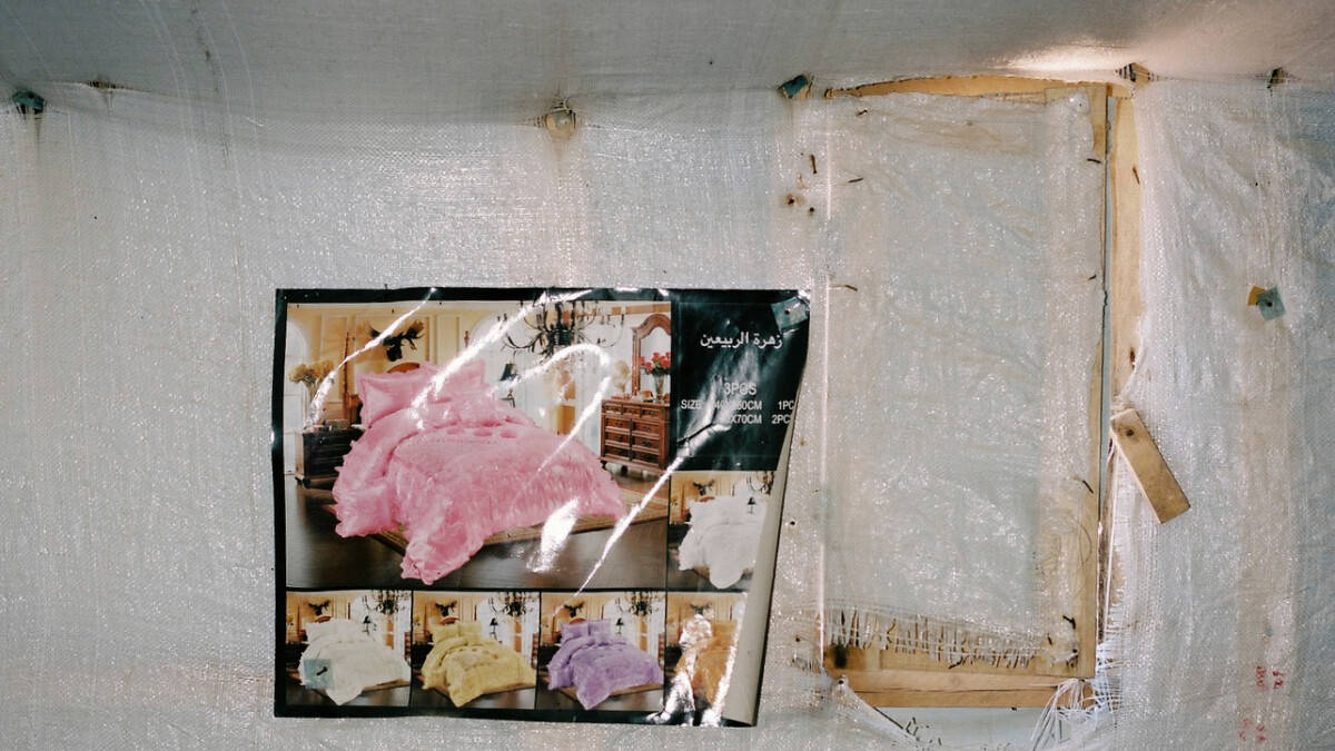 一對新婚夫妻在難民營陰暗且空蕩蕩的帳篷裡，掛著一幅華麗大床的照片。