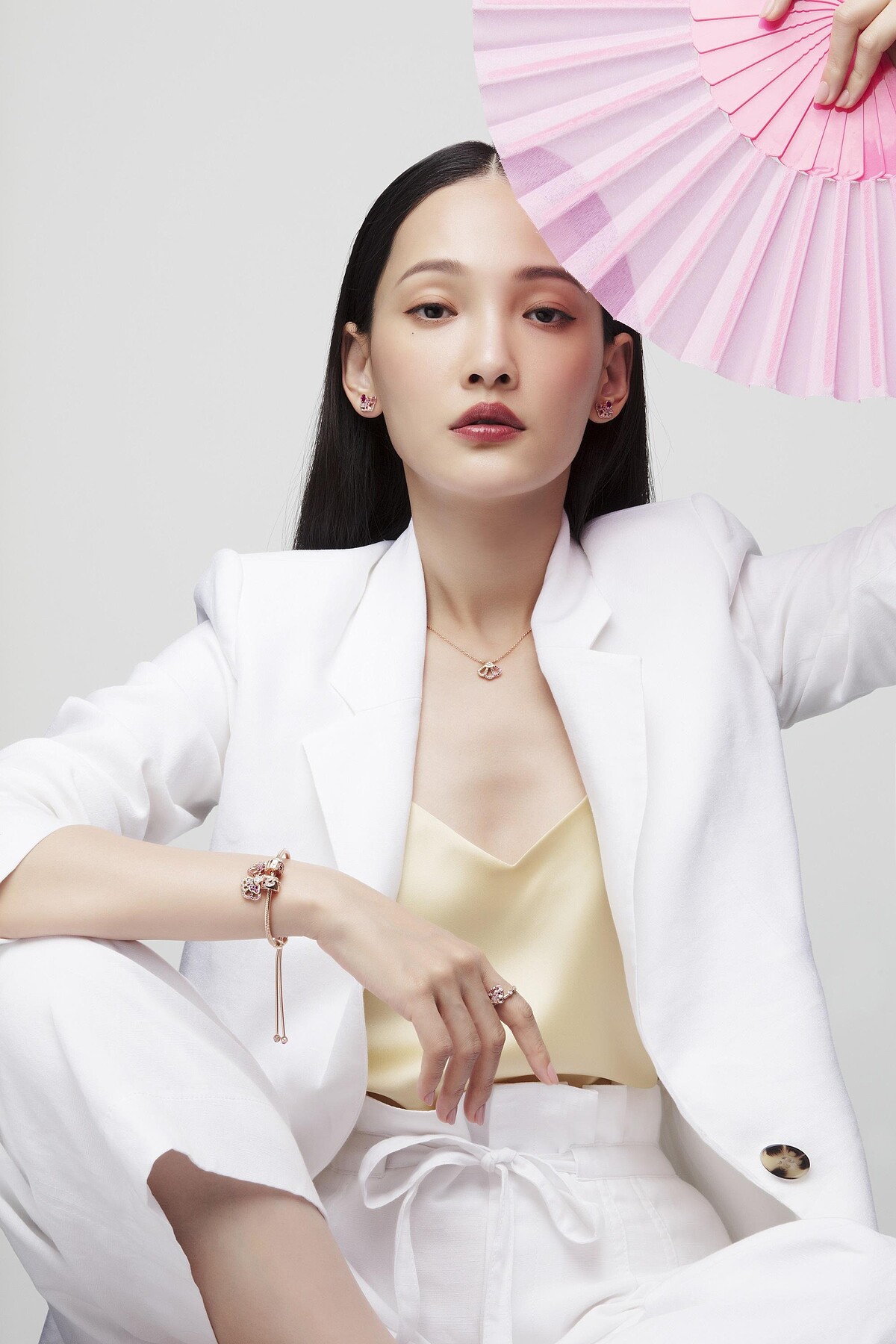 粉紅摺扇可拆式垂墜耳環，NT5,980、粉紅摺扇項鏈，NT5,380、粉紅摺扇戒指，NT5,380、粉紅摺扇手鏈，NT7,380、粉紅摺扇固定釦NT2,080、粉紅摺扇吊飾 NT3,280，手鏈，NT7,380 ，All by Pandora；白色棉麻面料西裝外套、長褲、奶油色絲緞背心，all by Club Monaco。