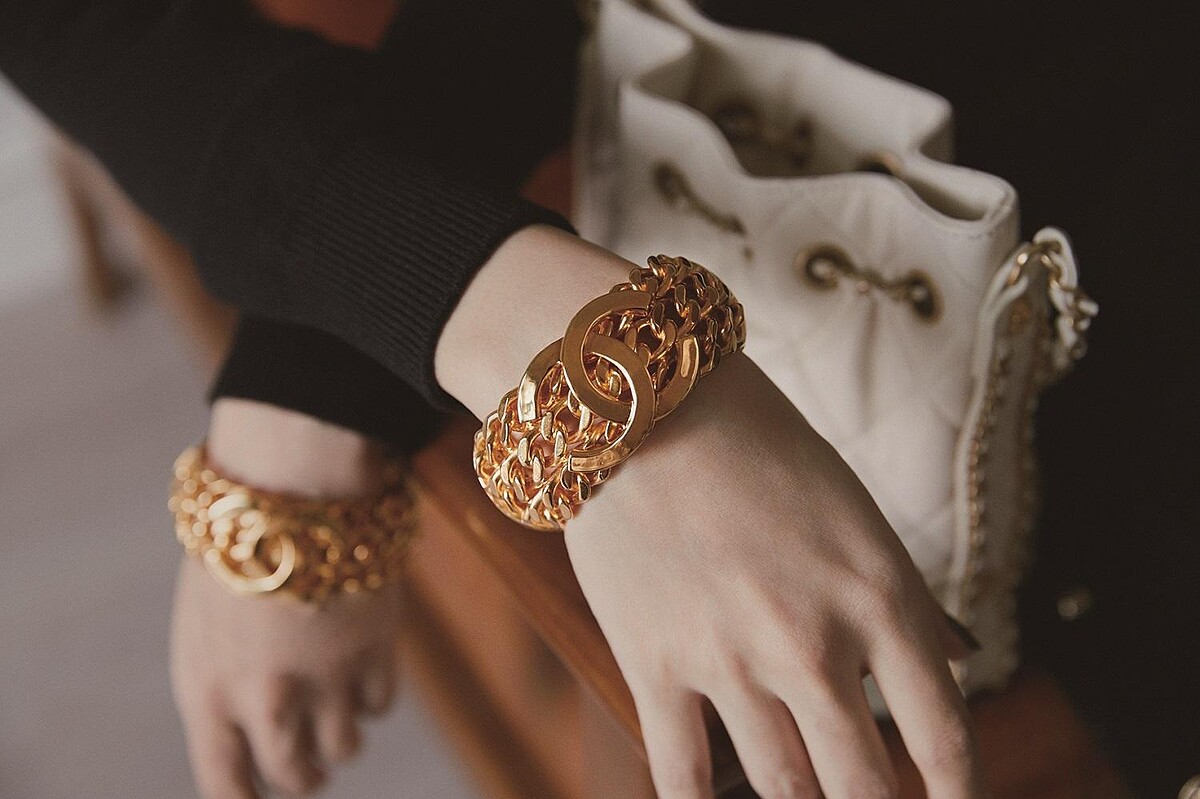 黑白拼接蕾絲緄邊洋裝、黑色十字造型高級樹脂手環、白色菱格紋皮革穿金屬鍊帶水桶包，CHANEL。