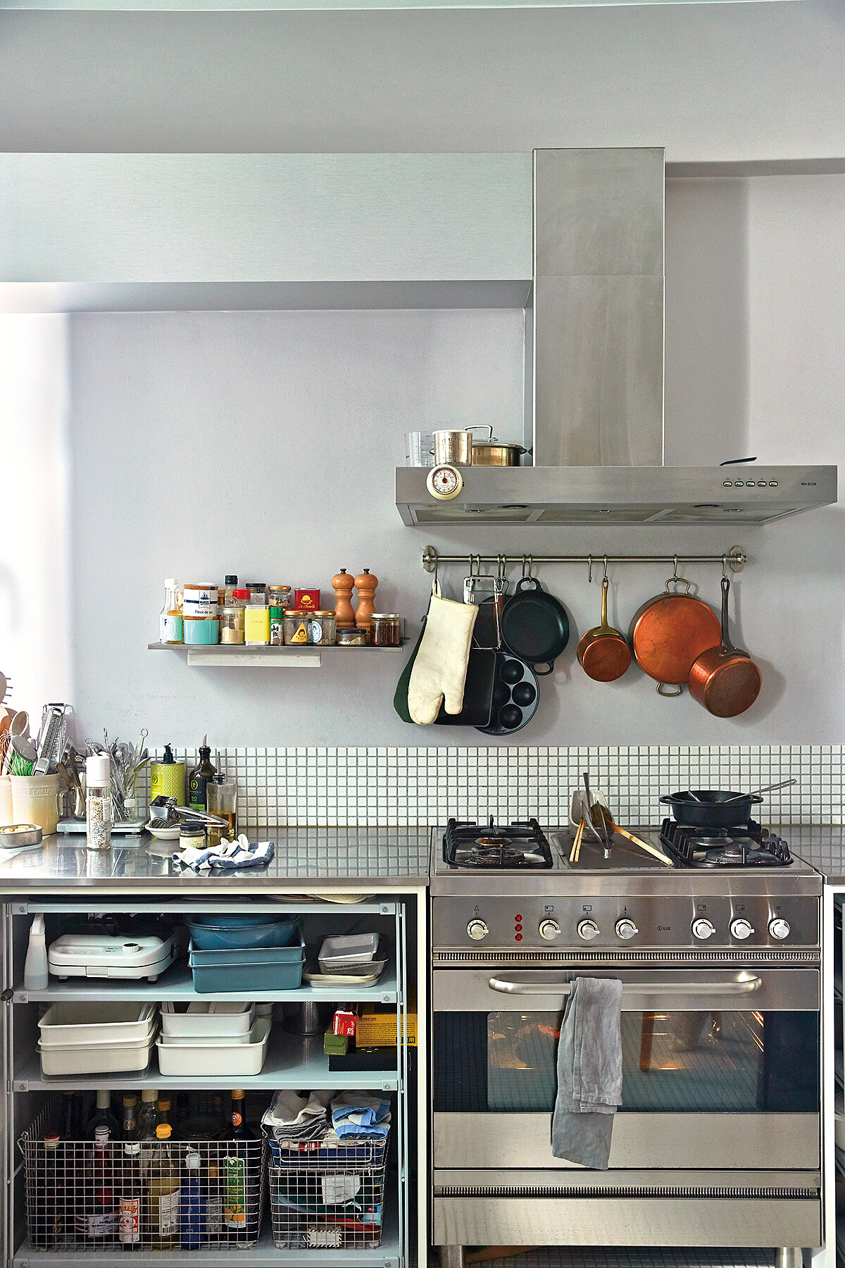 在牆面放上跟檯面一樣不鏽鋼材質的層板，把常用的調味料放在上面，以瓶身後高前低的擺法就可以清楚取用。