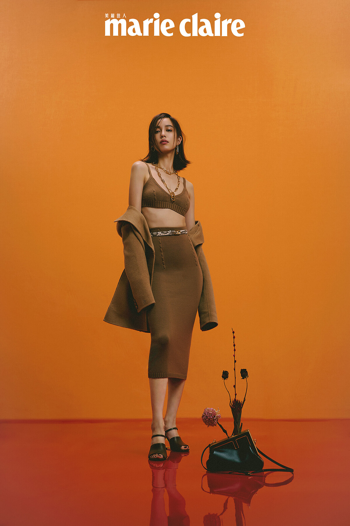 駝色針織短版上衣、針織A字裙、西裝領羊毛大衣、Fendi First F 字樣手拿包、Fendi First 咖啡色後跟倒F造型高跟涼鞋、造型耳環、Fendi O'Lock 造型長項鍊、Fendi O'Lock 造型頸鍊，all by Fendi