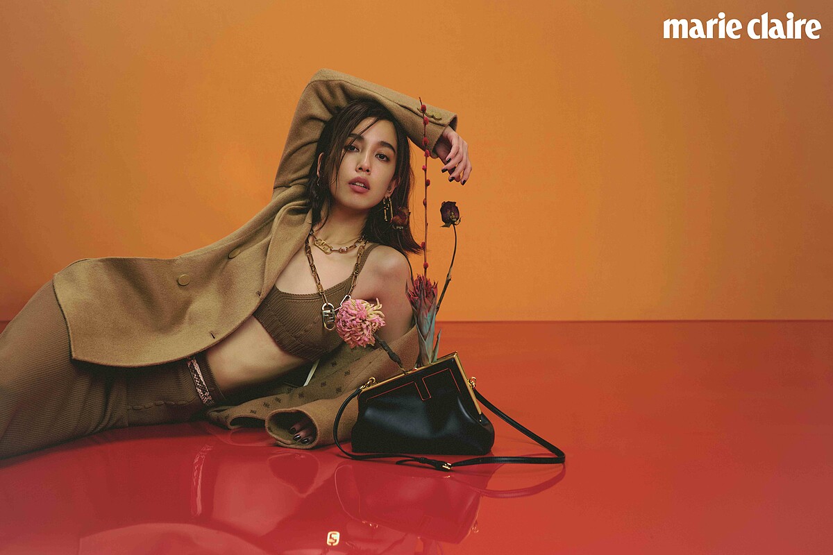 駝色針織短版上衣、針織A字裙、西裝領羊毛大衣、Fendi First F 字樣手拿包、Fendi First 咖啡色後跟倒F造型高跟涼鞋、造型耳環、Fendi O'Lock 造型長項鍊、Fendi O'Lock 造型頸鍊，all by Fendi