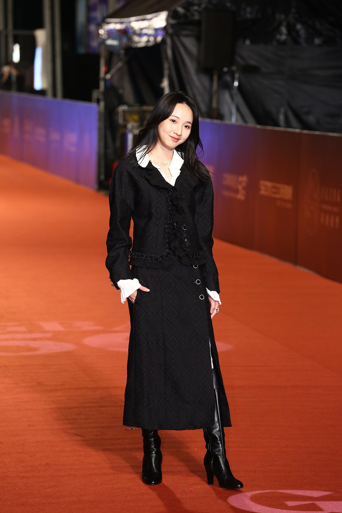 李沐身著Chanel 20/21工坊系列服飾:黑色羊毛真絲緹花,飾以刺繡荷葉緄邊外套與同款及膝開岔裙,配上率性的黑色皮革長靴。