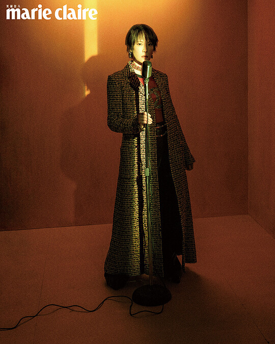 斜紋軟呢長版大衣、Logo 長袖上衣、酒紅色皮革長褲、吊墜耳環、金色 Logo 頸鍊、橘色串珠腰鍊、黃黑雙色皮革高跟鞋，all by CHANEL。