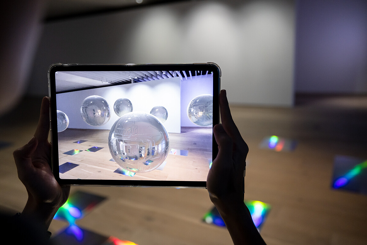 德國藝術家Martin Backes的AR創作〈我知道什麼？我只是個機器？！〉，讓觀眾透過行動裝置與懸浮在美術館空間內的正圓球形機器人相遇、對話 &copy;忠泰美術館