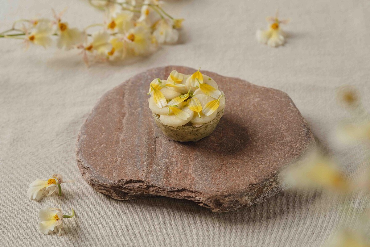 「蛤蠣、筊白筍、番茄」-經典的新鮮蛤蜊，加入了茭白筍和發酵番茄高湯凍，層層鋪疊，融合出細膩馥郁的風味，再點綴以黃色的茼蒿花，增添視覺和味覺的雙重享受。檸檬皮碎與巴西里油的細緻點綴，為這道菜帶來一絲清新的口感。薄脆的塔殼與帶有鮮味的澄清番茄凍完美結合，為您呈現夏日的清新美味。