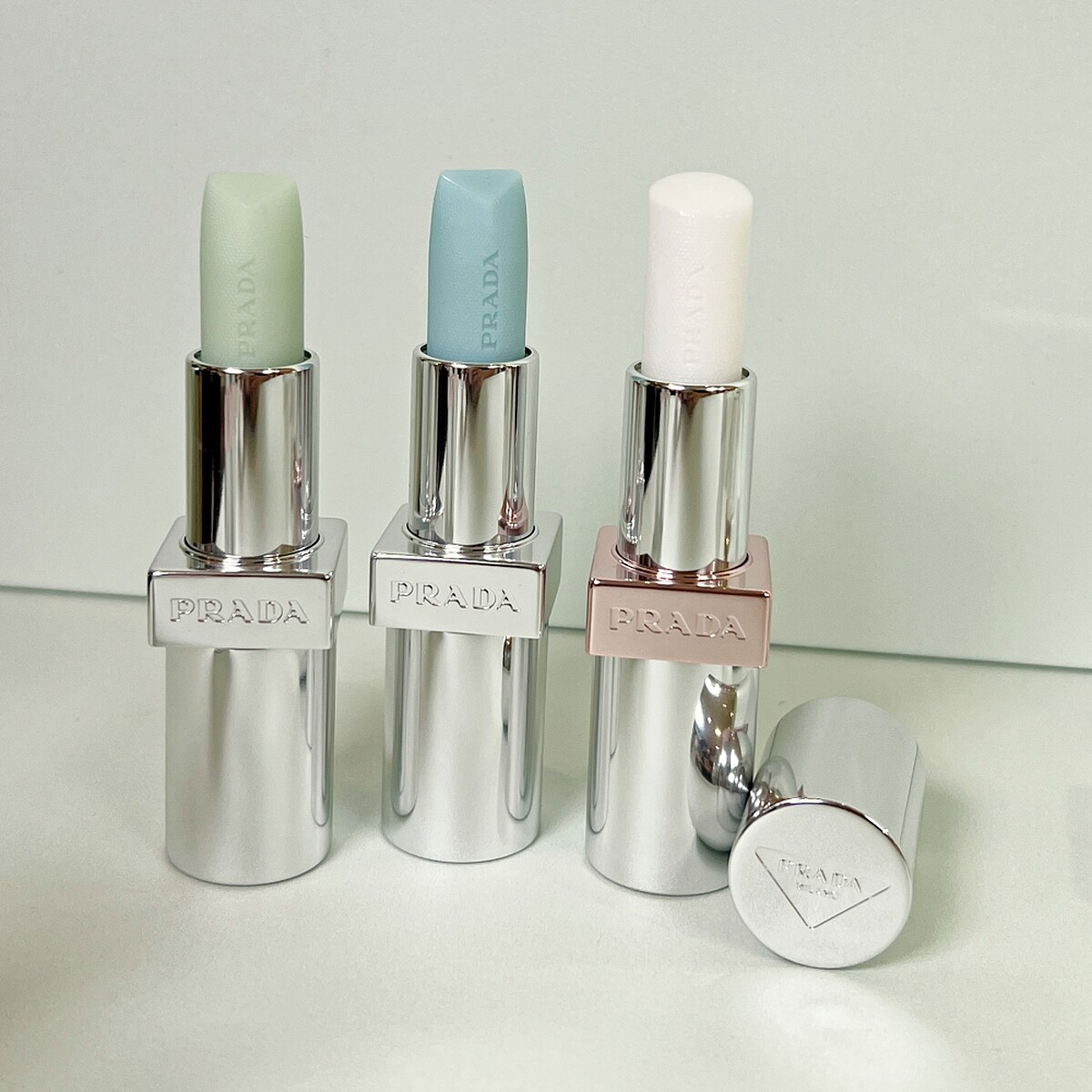 PRADA(左起)經典潤唇膏# U001莫測藍、U000顛覆綠、原生稜光水唇膏#U014幻光白。