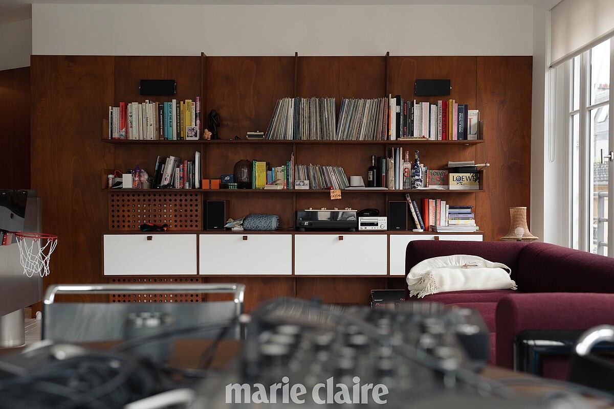 從餐桌可以看到整個客廳區,左邊有 Adam 的籃球框,右邊是勃根地色沙發。書架上有待整理的唱片專輯、物件收藏,像是 Louise 的寶物展示櫃一樣。