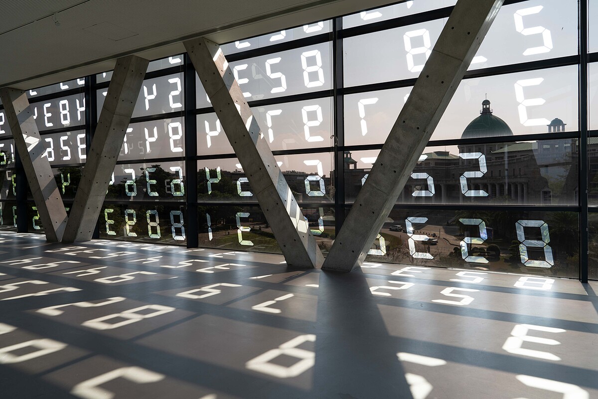 宮島達男為亞美館現地量身打造的〈變化地景／變化美術館〉，於窗面貼上從輪盤隨機轉出的數字。隨著陽光移動，光影與數字交織為日晷般的時間痕跡。