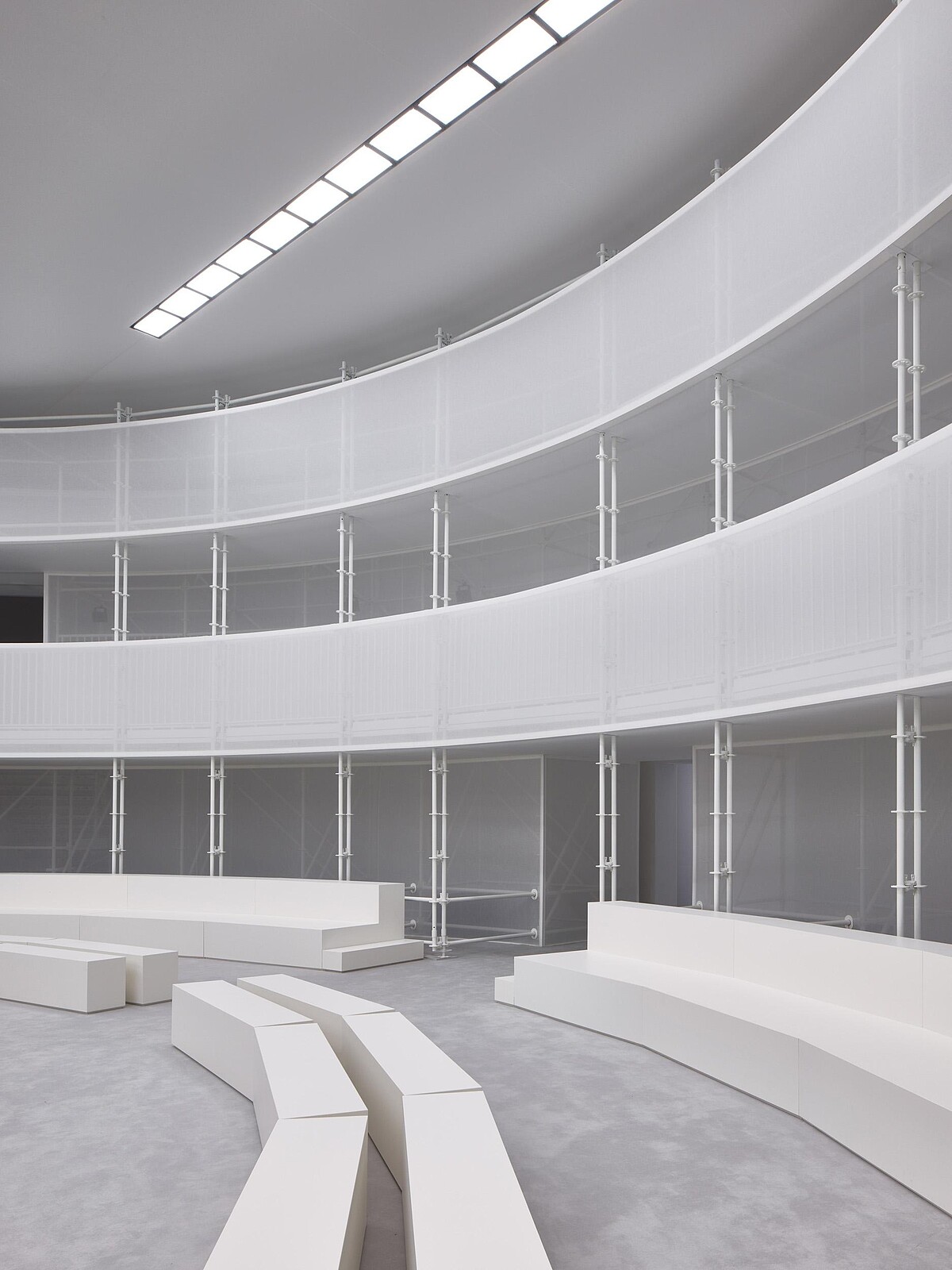 Loewe 2027春夏大秀選址巴黎文森城堡,由Casper Mueller Kneer Architects打造的臨時橢圓劇場,以外露結構與通透的白色帷幕構築純淨空間,讓服裝的輪廓、材質與細節成為視覺焦點。